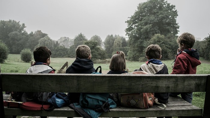 Kinder sitzen auf einer Bank im Park und schauen in die Ferne.