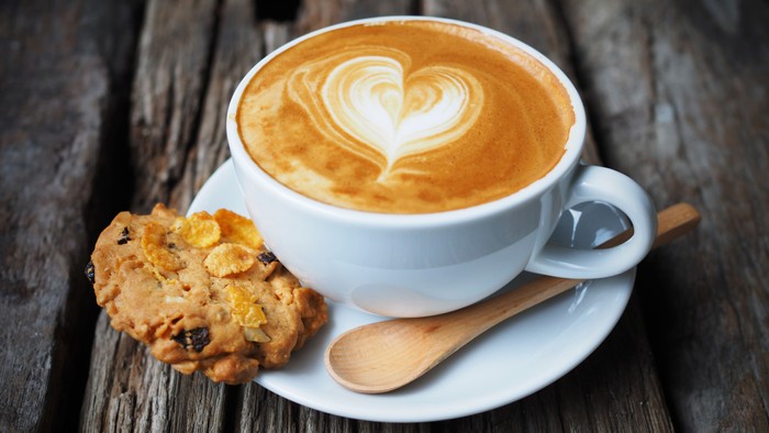 Ein Cappuccino mit Herzverzierung und ein Keks auf einem Holztisch