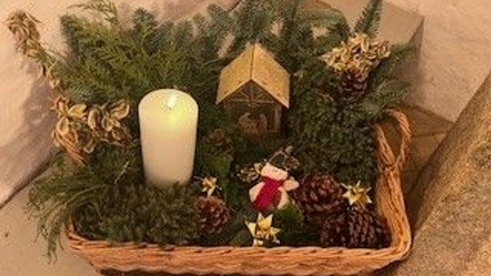Flettet kurv som feriecenterstykke med fyr, lys, kogler og lille træhusdekoration.