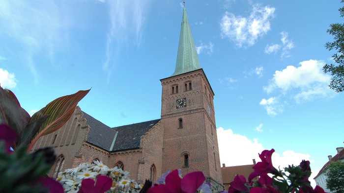 En kirke med højt tårn og blomster i forgrunden
