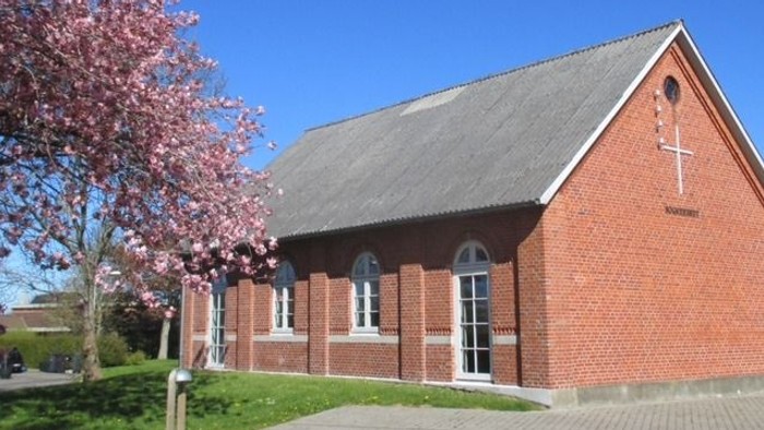 En rød murstenskirke med kryds og blomstrende træ foran