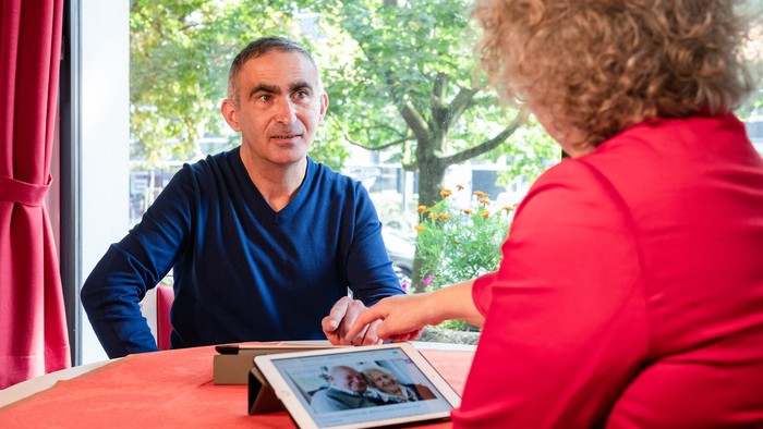 Ein Mann und eine Frau sitzen an einem Tisch und schauen auf ein Tablet.