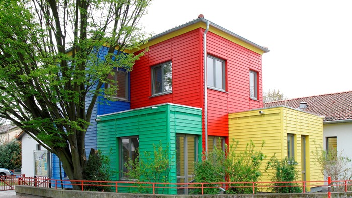 Buntes, mehrfarbiges Haus mit rotem, grünem und gelbem Anstrich, umgeben von Bäumen und einem Zaun.