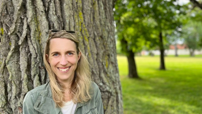 En kvinde med blond hår står ved et træ i en park.