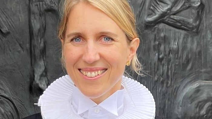 Kvinde med hvid krage og sort jakke står foran skulptur.