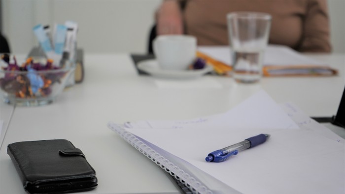 En skrivebord med notebog, pen, telefon og en kop kaffe.
