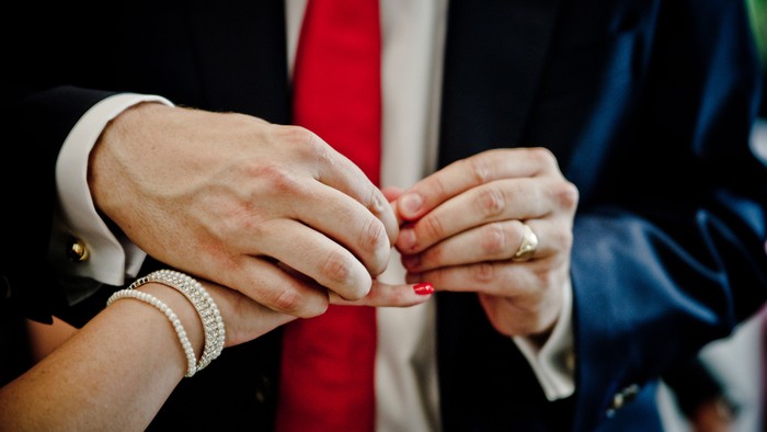 Zwei Personen tauschen Ringe aus, eine trägt eine Armbanduhr.