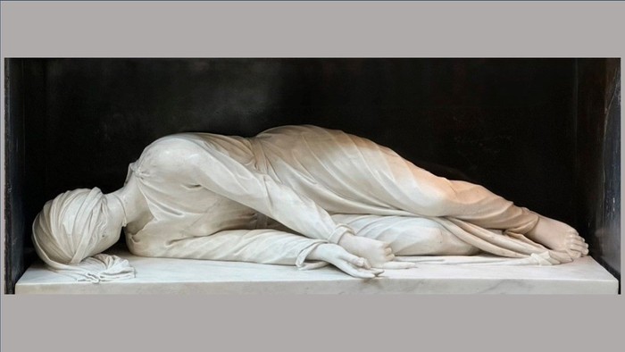 Die Statue zeigt eine liegende, in Tuch gehüllte Gestalt.