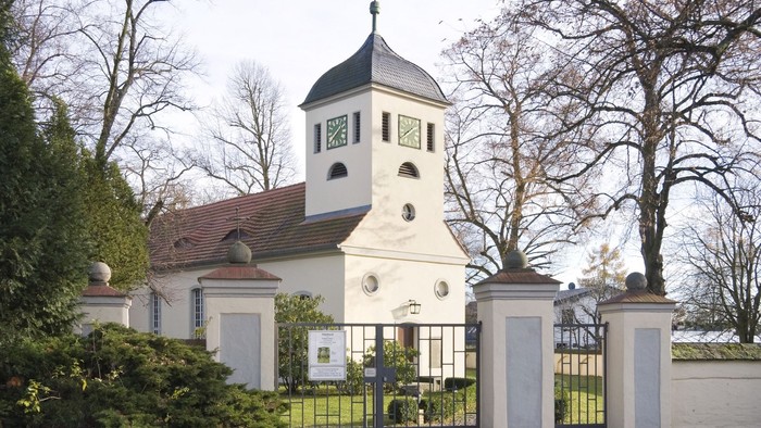 Weißes Gebäude mit Uhrturm und schwarzem Dach hinter hohem Tor
