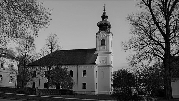 Kirchengebäude mit hohem Turm und Uhr, umgeben von Bäumen