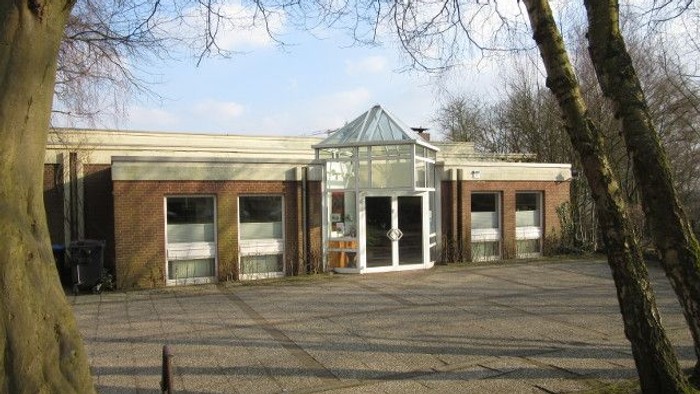 Das Bild zeigt ein modernes Gebäude mit Glasfront und Terrasse, umgeben von kahlen Bäumen und einem klaren Himmel.