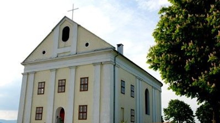 Ein weißes Kirchengebäude mit Kreuz auf dem Dach, umgeben von Bäumen.