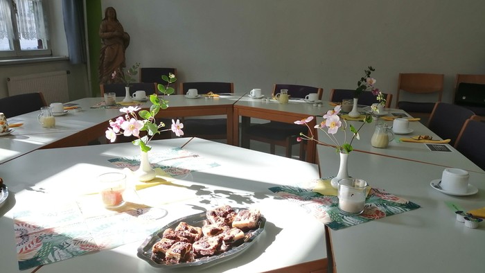 Ein helles Zimmer mit mehreren Tischen, die mit Blumen, Geschirr und Gebäck gedeckt sind
