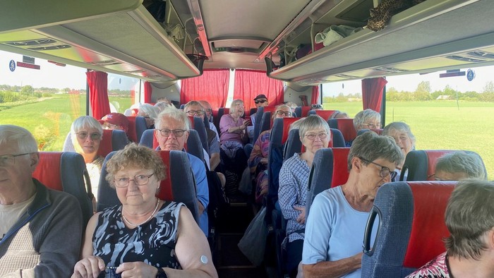 En gruppe ældre personer sidder i en rød bus.