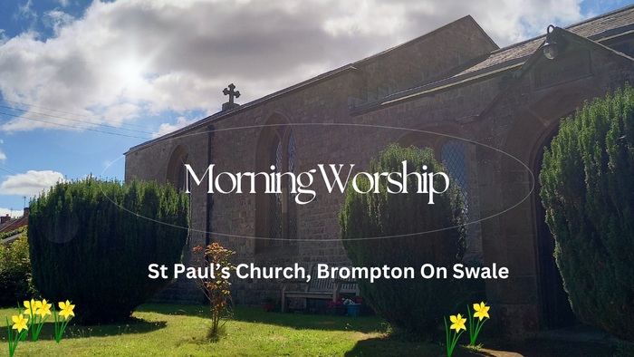 Church building with cross on top, surrounded by greenery and flowers, under a partly cloudy sky