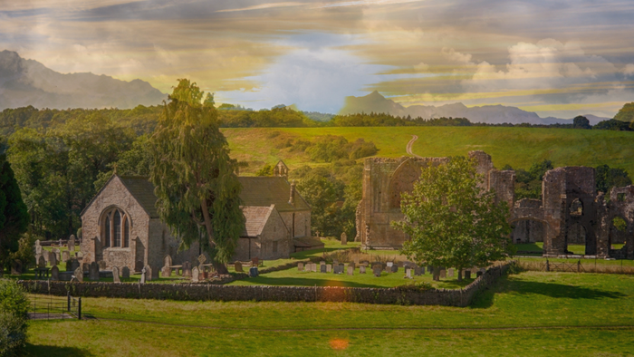 Rural landscape with old church and ruins, surrounded by green fields and trees.