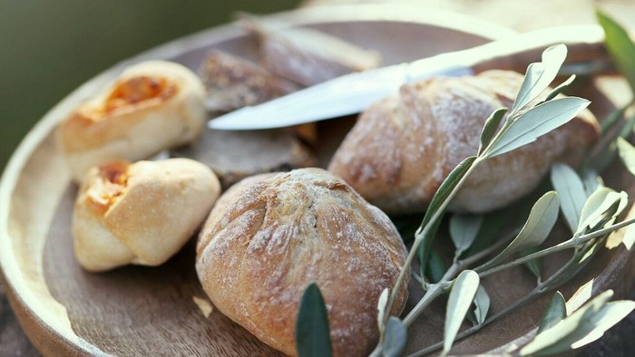 Teller mit frischgebackenen Brötchen, einem Messer und einem Olivenzweig