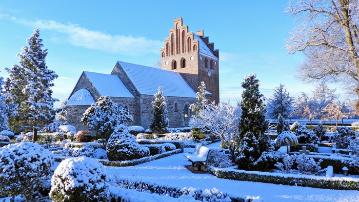 Snedækket have og kirke under klar blå himmel