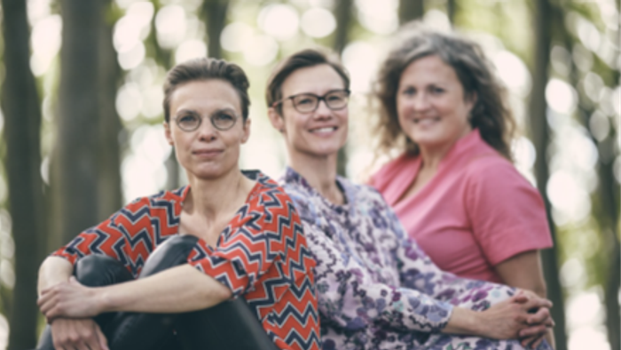 Tre kvinder står sammen i skoven og smiler til kameraet.