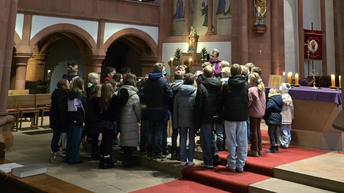 Gruppe von Menschen in einer Kirche versammelt, einige halten Kerzen, mit religiösen Dekorationen im Hintergrund.