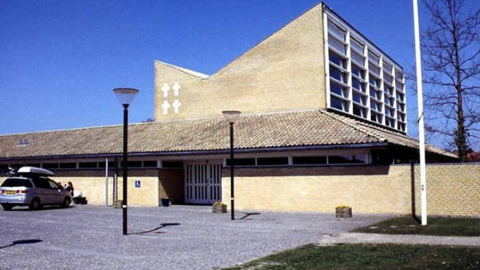 Moderne kirke med store vinduer og en bil parkeret i nærheden.