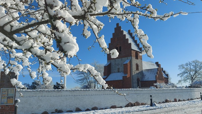 En snedækket kirke med tårn og en bil på en snedelegede vej