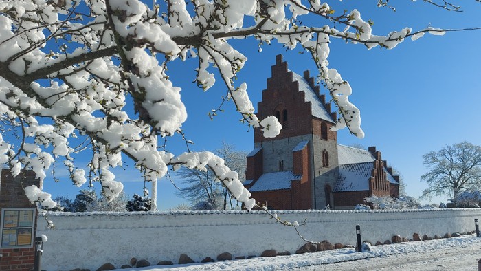 En snedækket kirke med tårn og en bil på en snedelegede vej