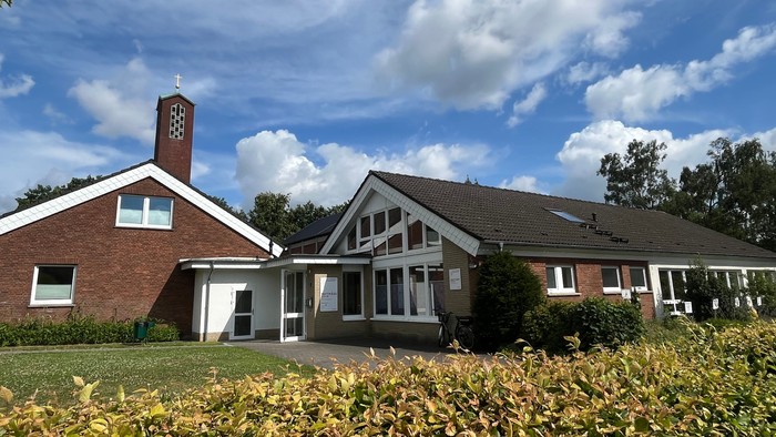 Man sieht links das rot geklinkerte Pfarrhaus, rechts schließt das Gemeindehaus mit vielen weißen Fenstern an. Im Hintergrund sieht man noch den Turm der Matthäuskirche.