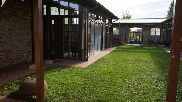 nnenhof mit Rasen, umgeben von Backsteinmauern und Gebäuden mit großen Fenstern und Holzbalken.