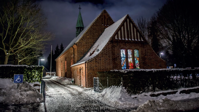 En sneet dækket sti fører til en lille, oplyst kirke med et tårnspir.
