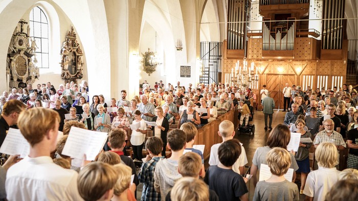 En stor kirkefuld af mennesker, der synger og holder noter.