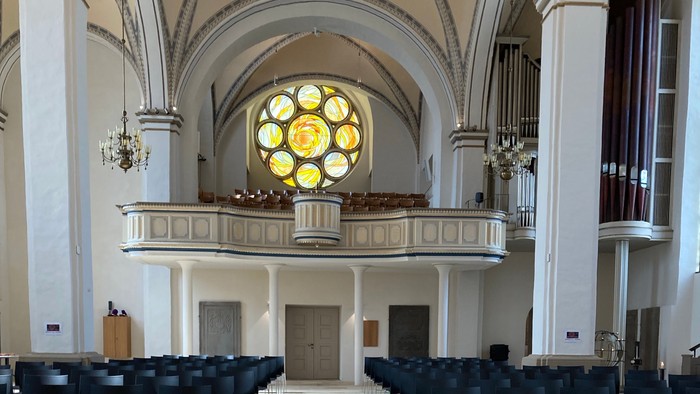 In der Kirche steht ein Blumenarrangement vor dem Altar, umgeben von Stühlen.