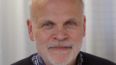 En bald, eldre mand med skæg og blå stribede skjorte under en sort trøje.