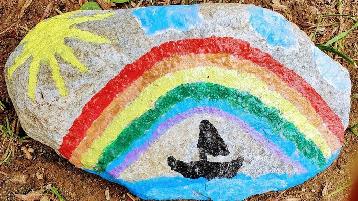 Bunter Regenbogen auf einem Stein gemalt, darunter eine schwarze Katze