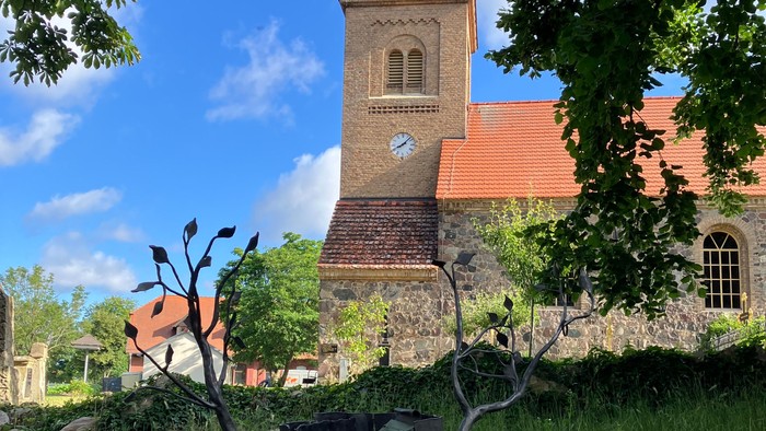 Kirchturm mit Uhr, davor Skulptur im Park