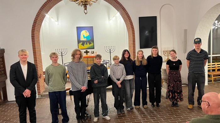 Gruppe af mennesker, der holder menoraer i en synagoge under en ceremoniel sammenkomst.