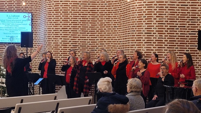 Et kor optræder på scenen med publikum sæt i rækker.