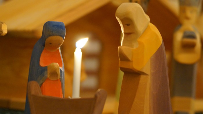 En træudskåret julekrybbe med Maria, Josef og baby Jesus i en krybbe, oplyst af et stearinlys.