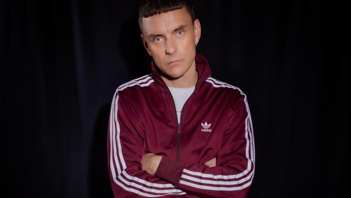 En ung mand i rød sportssuit sidder med armene krydset på et keyboard.