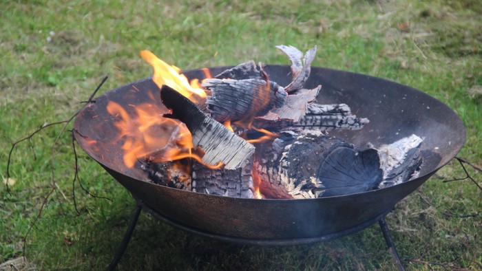 Bålfad med brændende træstykker på græsplæne