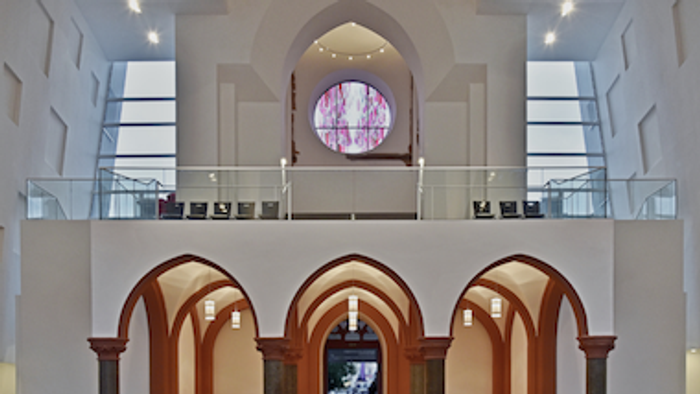 Das Bild zeigt den Innenraum einer modernen Kirche mit hohen Decken, Rundbogenfenstern und einem großen Rundfenster.