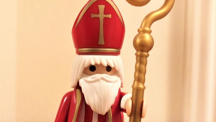 Eine Spielzeugfigur des Heiligen Nikolaus mit goldenem Stab und Buch, gekleidet in Bischofsgewand.