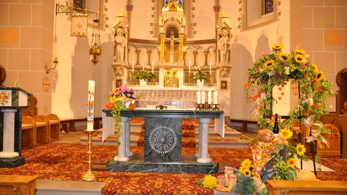 Innenraum einer Kirche mit Altar, Kerzen und Blumenarrangements