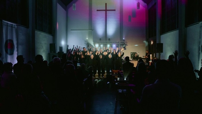 Gottesdienst mit Gemeinde, die in einer hell erleuchteten Kirche während einer nächtlichen Versammlung die Hände erhebt.