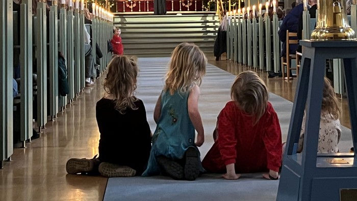 Tre børn sidder i en kirke.