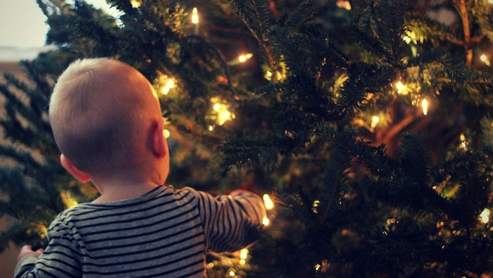 Ein Baby schaut fasziniert in den Weihnachtsbaum.