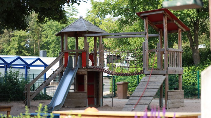 Ein Kinderspielplatz mit Rutschen, Klettergerüsten und hölzernen Spieltürmen in einer grünen Parkanlage.