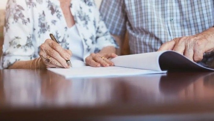 To personer underskriver dokumenter ved et bord under det, der ser ud til at være en formel aftale eller møde.