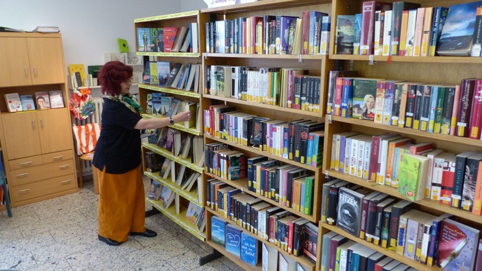 Eine Person, die in einem gemütlichen Bibliotheksraum bunte Bücherregale mit verschiedenen Büchern durchstöbert.