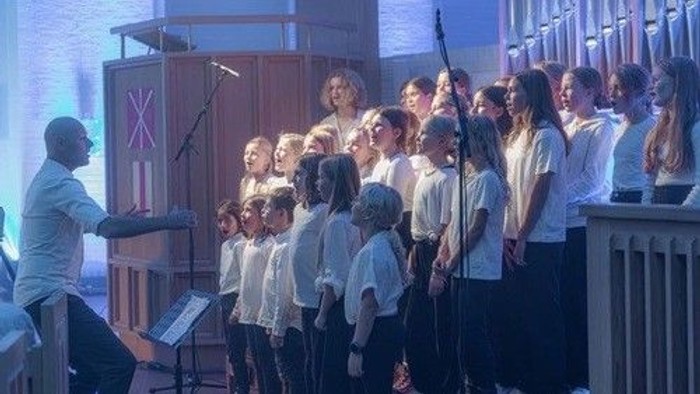 En gruppe børn synger i en kirke med en mand til stede.